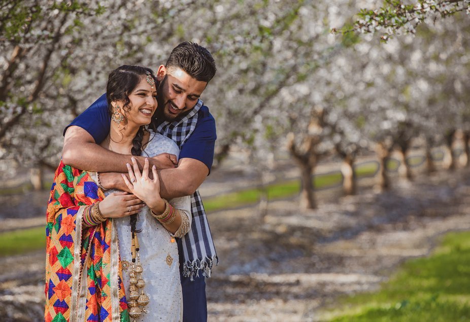 Happy engaged couple hold each other and smile while in the Yuba City's Almond Orchards